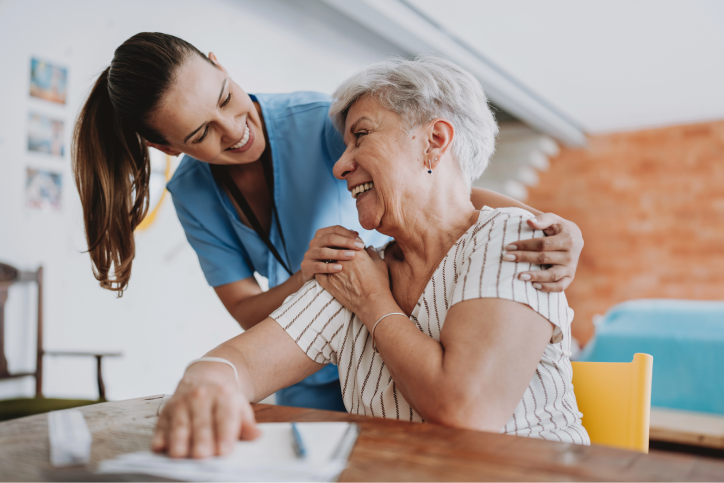 An APP smiles and hugs her seated patient’s shoulders
