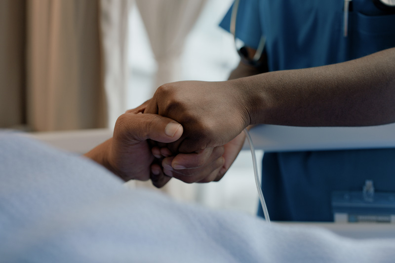 A nurse holding a patient's hand in a hospital setting, symbolizing support and compassionate care.