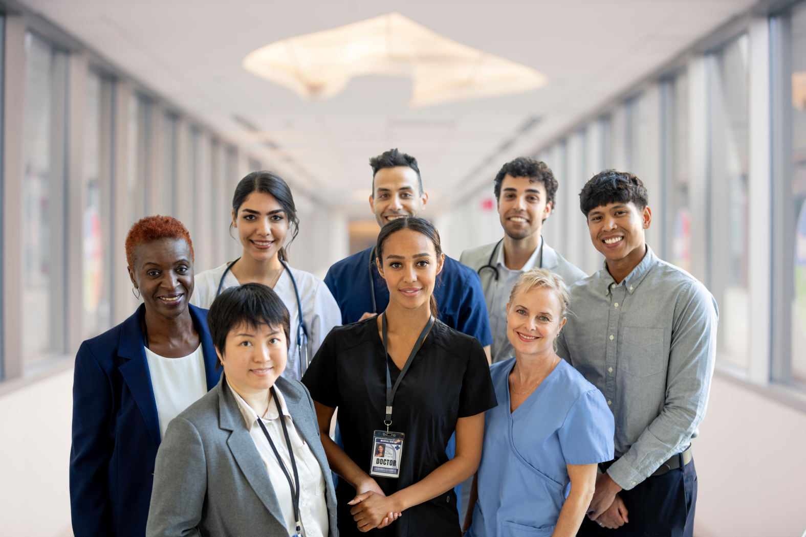A group of Riverside Healthcare team members standing together in a bright hospital hallway, smiling and representing a variety of clinical and support roles.