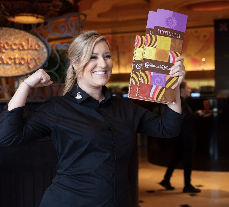 Smiling female line cook proudly showing off a dish she made in the kitchen.
