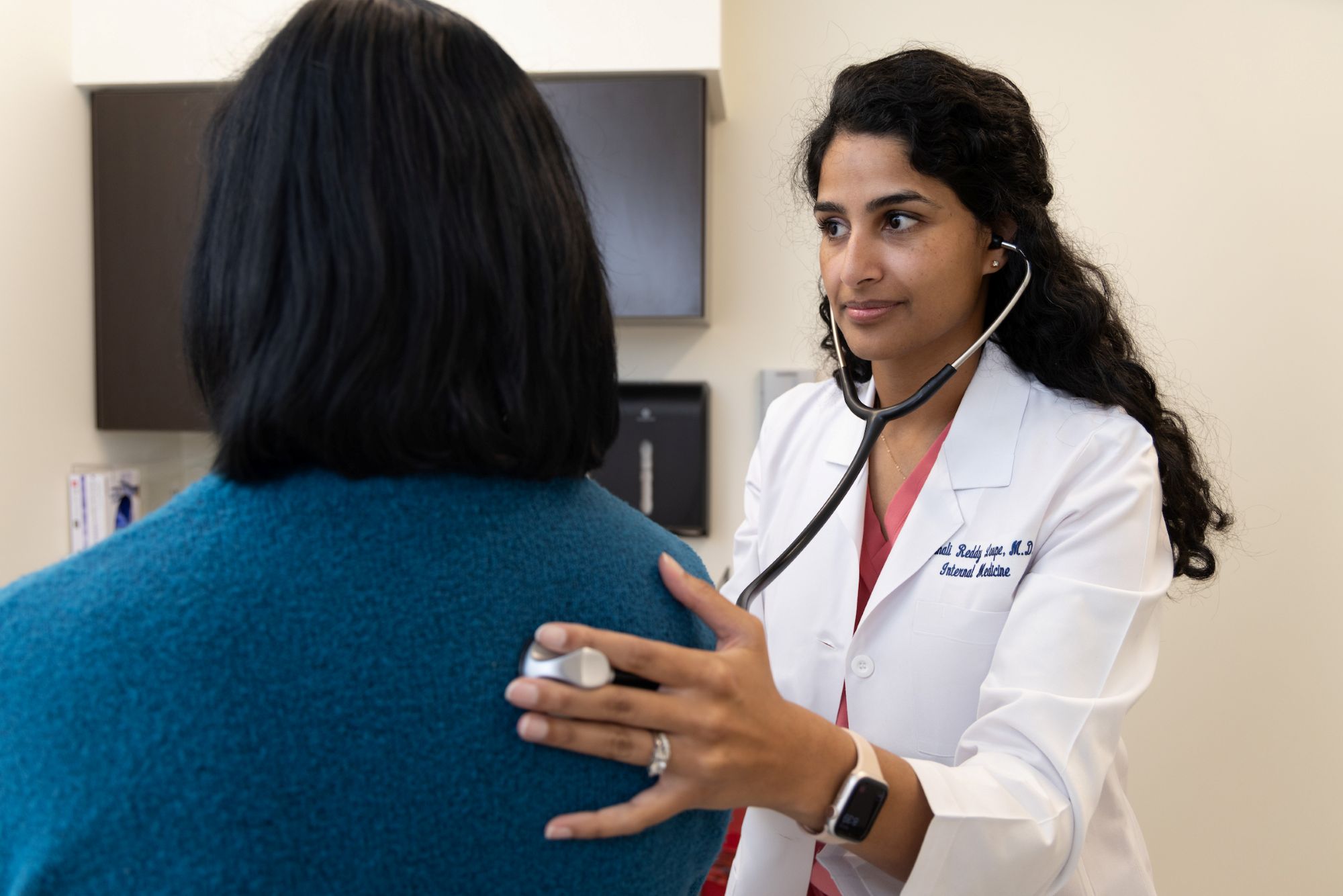 A male doctor wearing a white coat and stethoscope that is being used on a female patient.