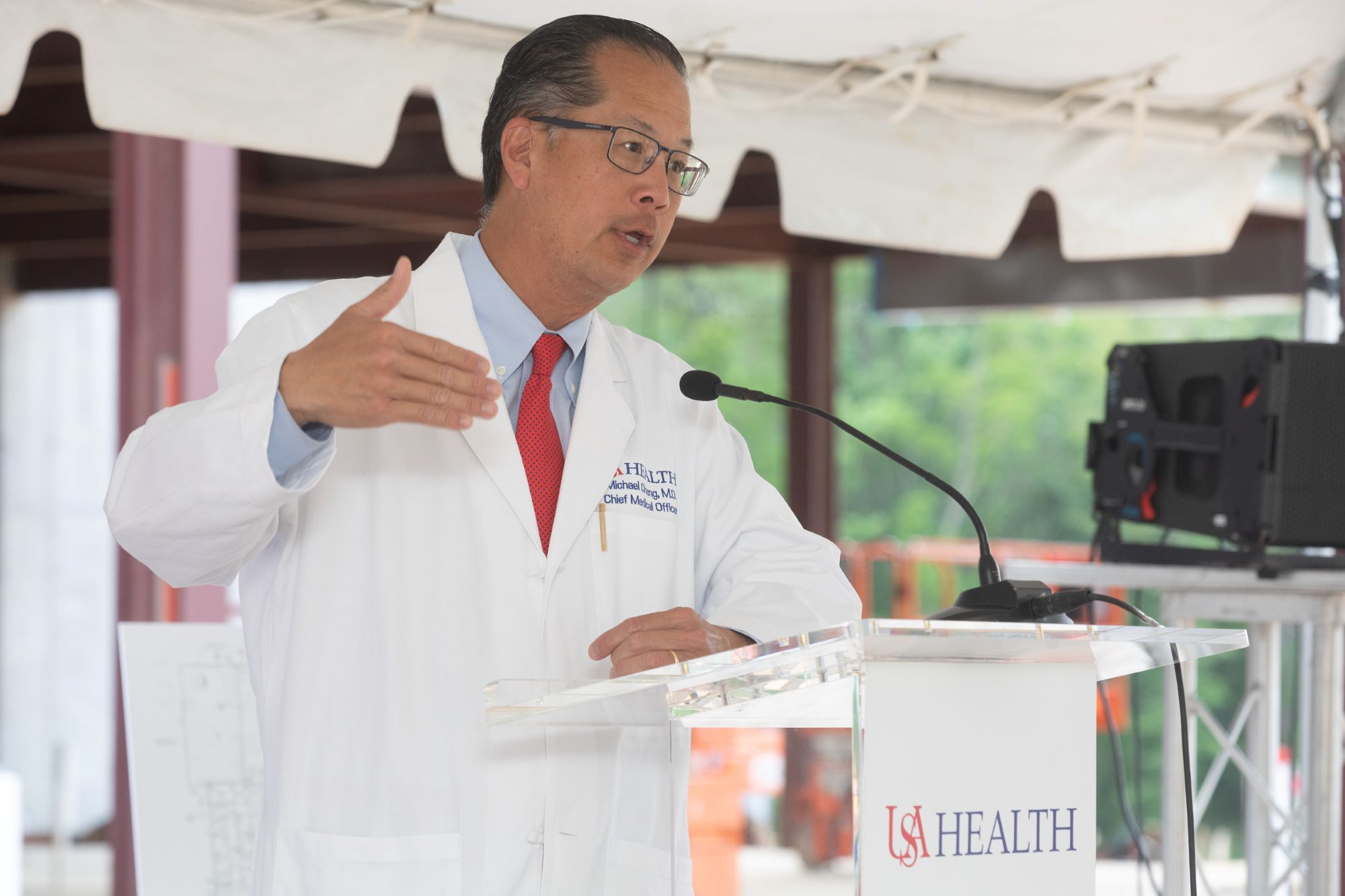 A man wearing a suit and a tie standing in front of a podium with a USA Health logo and giving a speech.